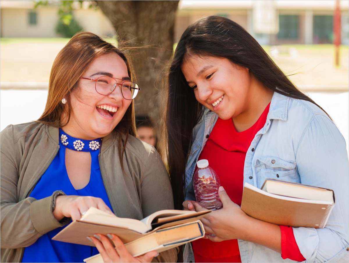 Two Native female students looking at a book and smiling